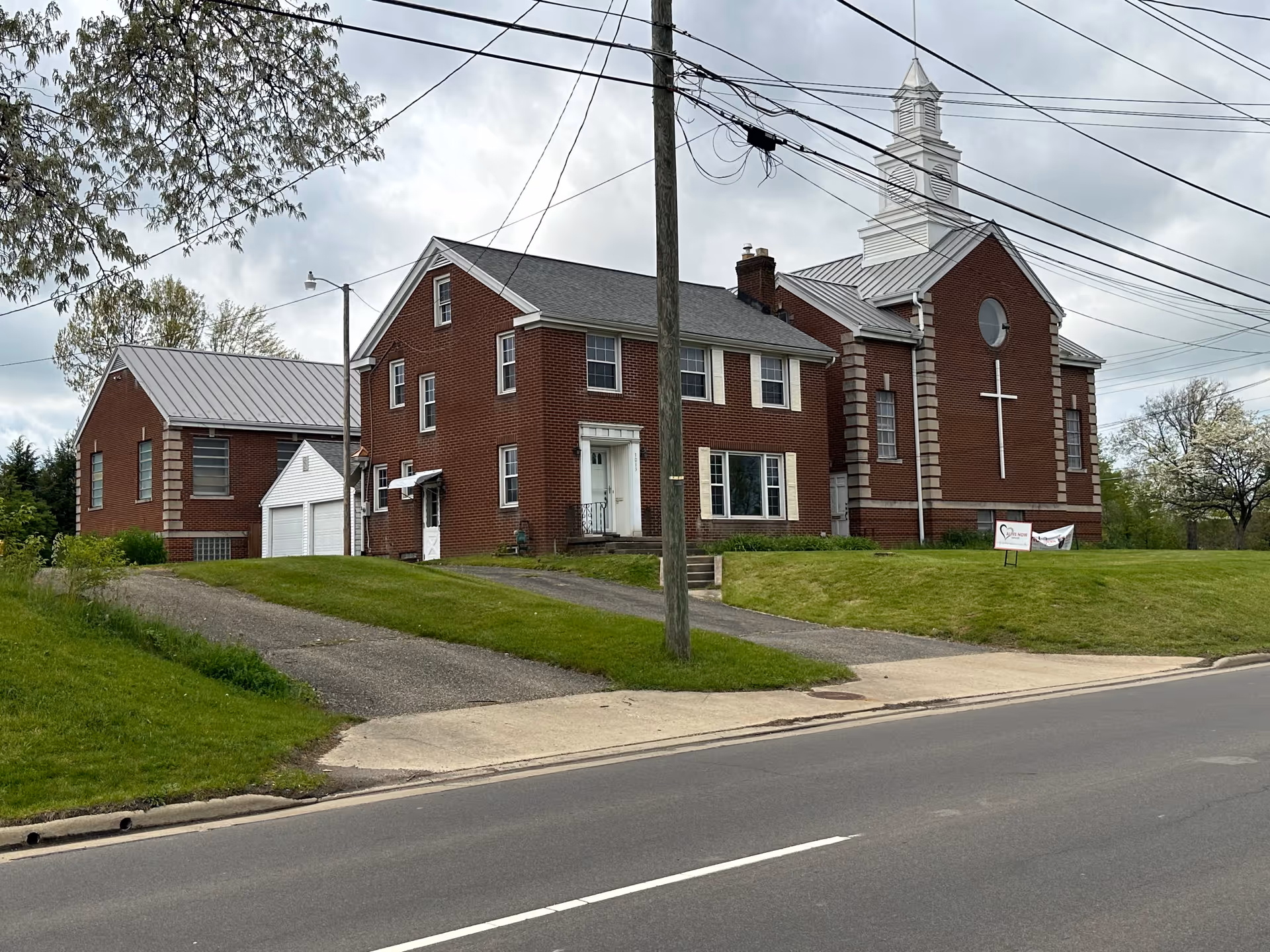 Brick senior living facility with a cross on the facade sits along a grassy street frontage.