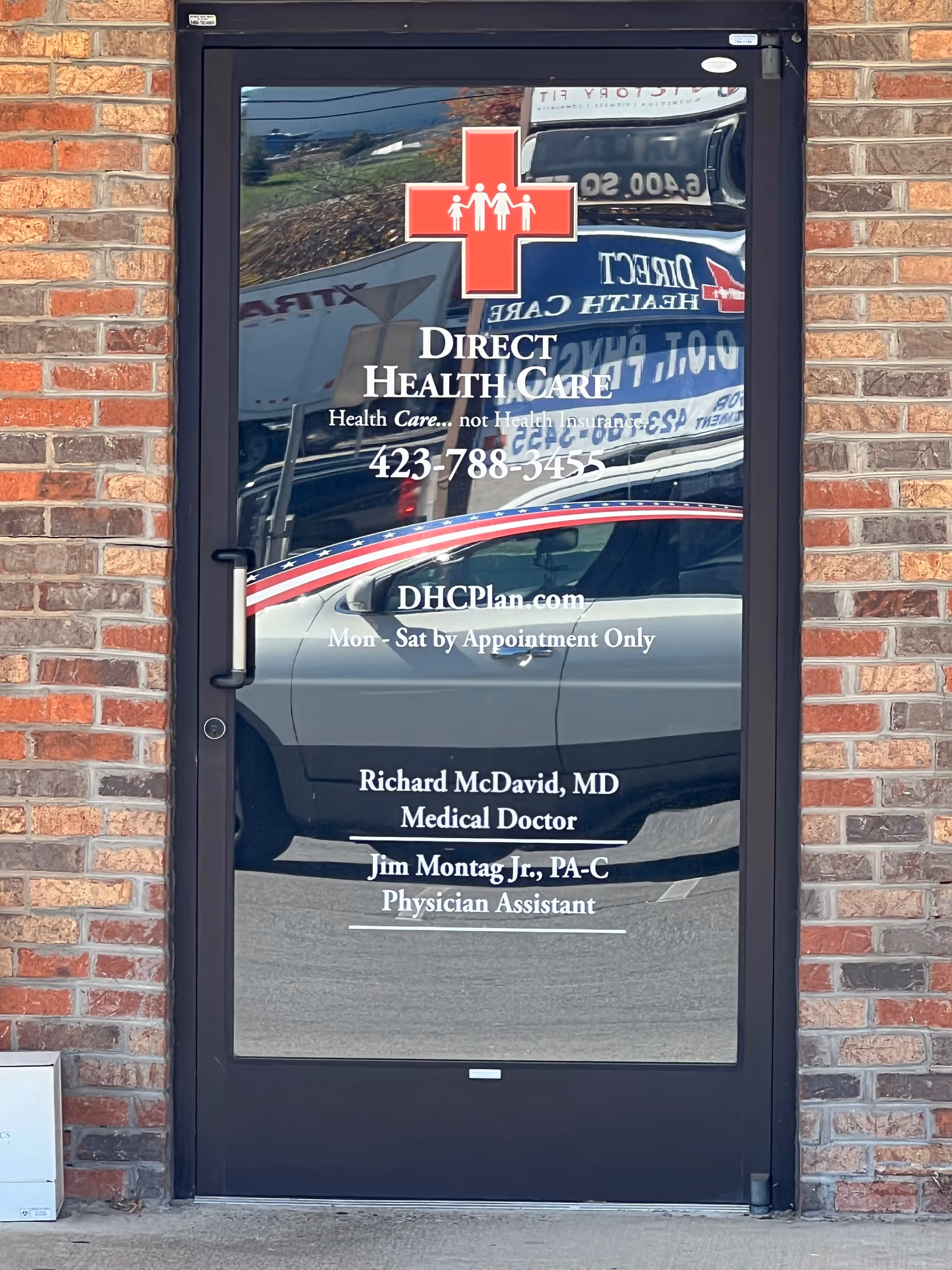 Glass entrance door with Direct Health Care logo and contact details on brick wall.