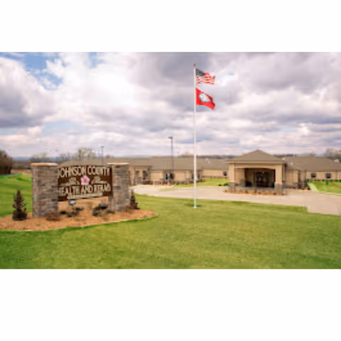 Exterior view of Johnson County Health and Rehab facility with sign, flagpole, and lawn.
