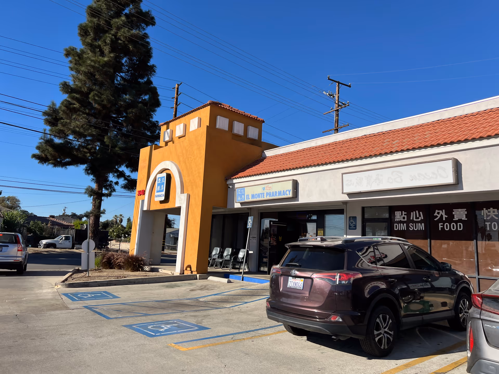 Orange-tinted front of a strip mall with El Monte Pharmacy and parked cars.