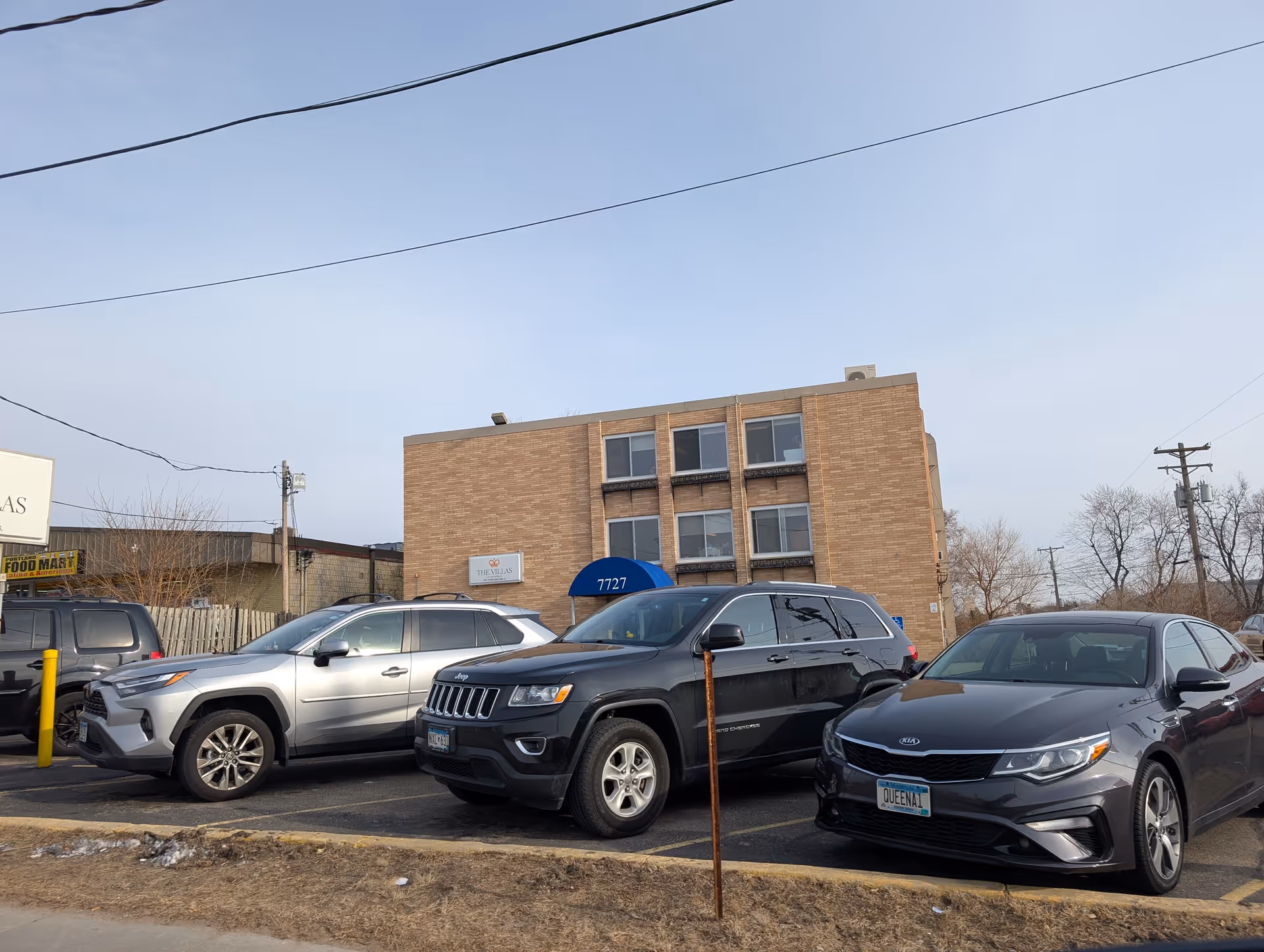 Three-story brick building with a blue awning and several cars parked in front.