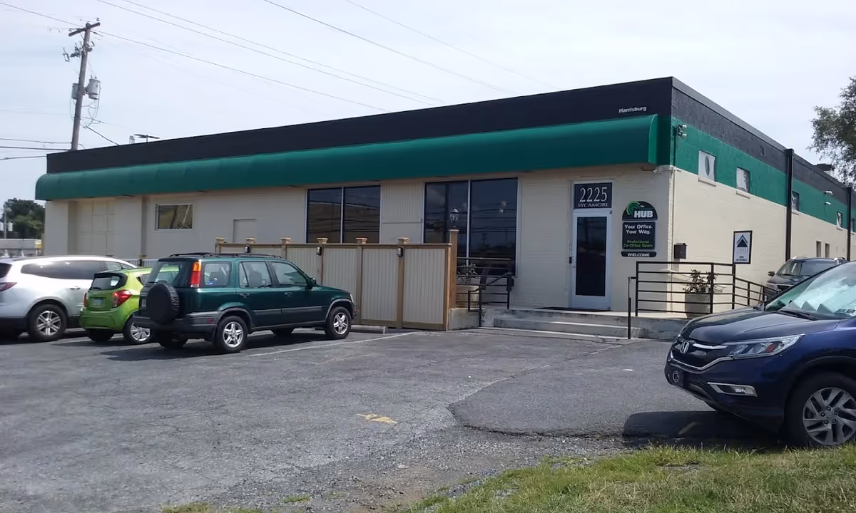 Exterior of a beige building with a green awning, parking lot, and signage.