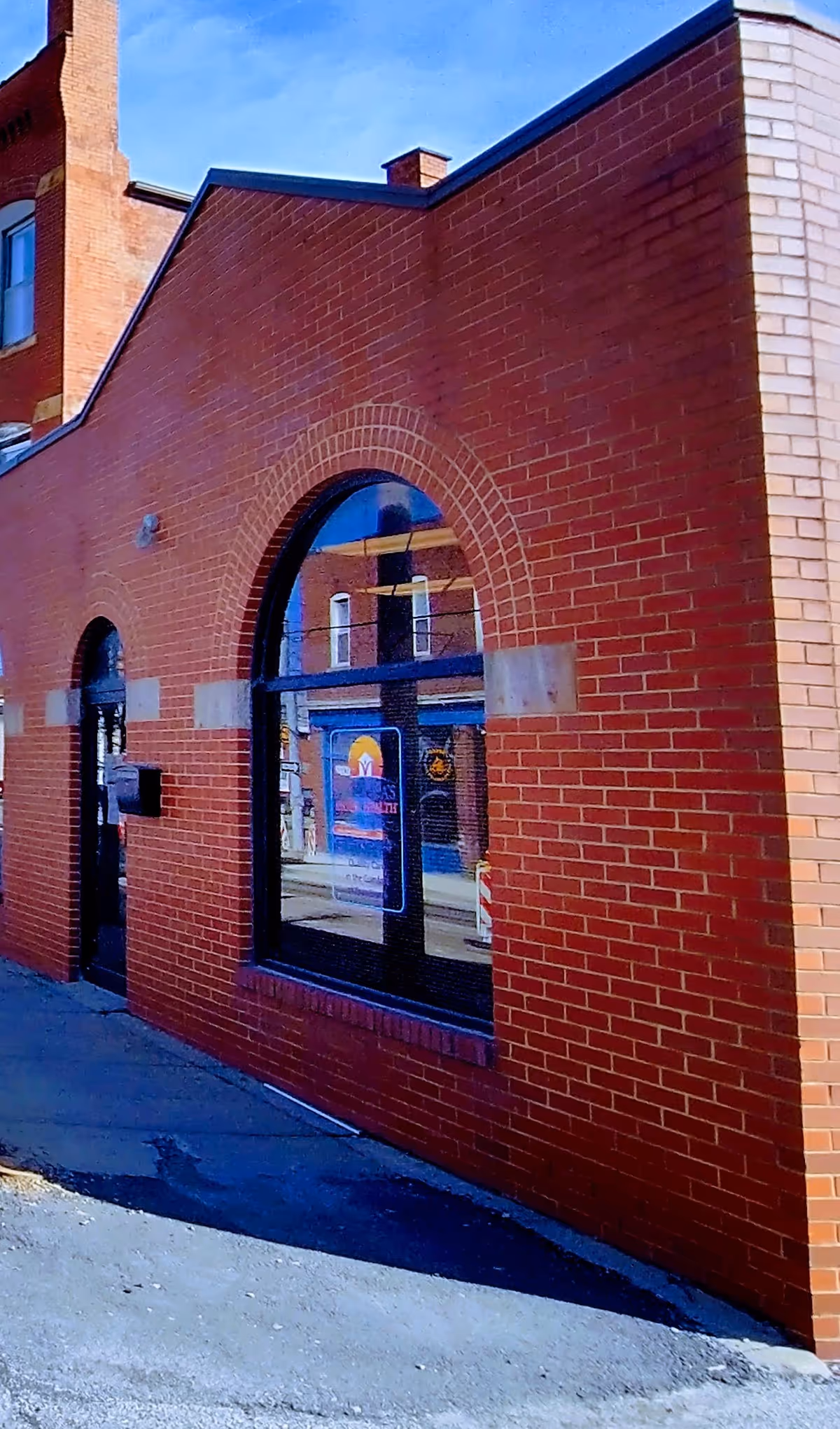 Brick building exterior with arched window and storefront reflections on a sunny day.