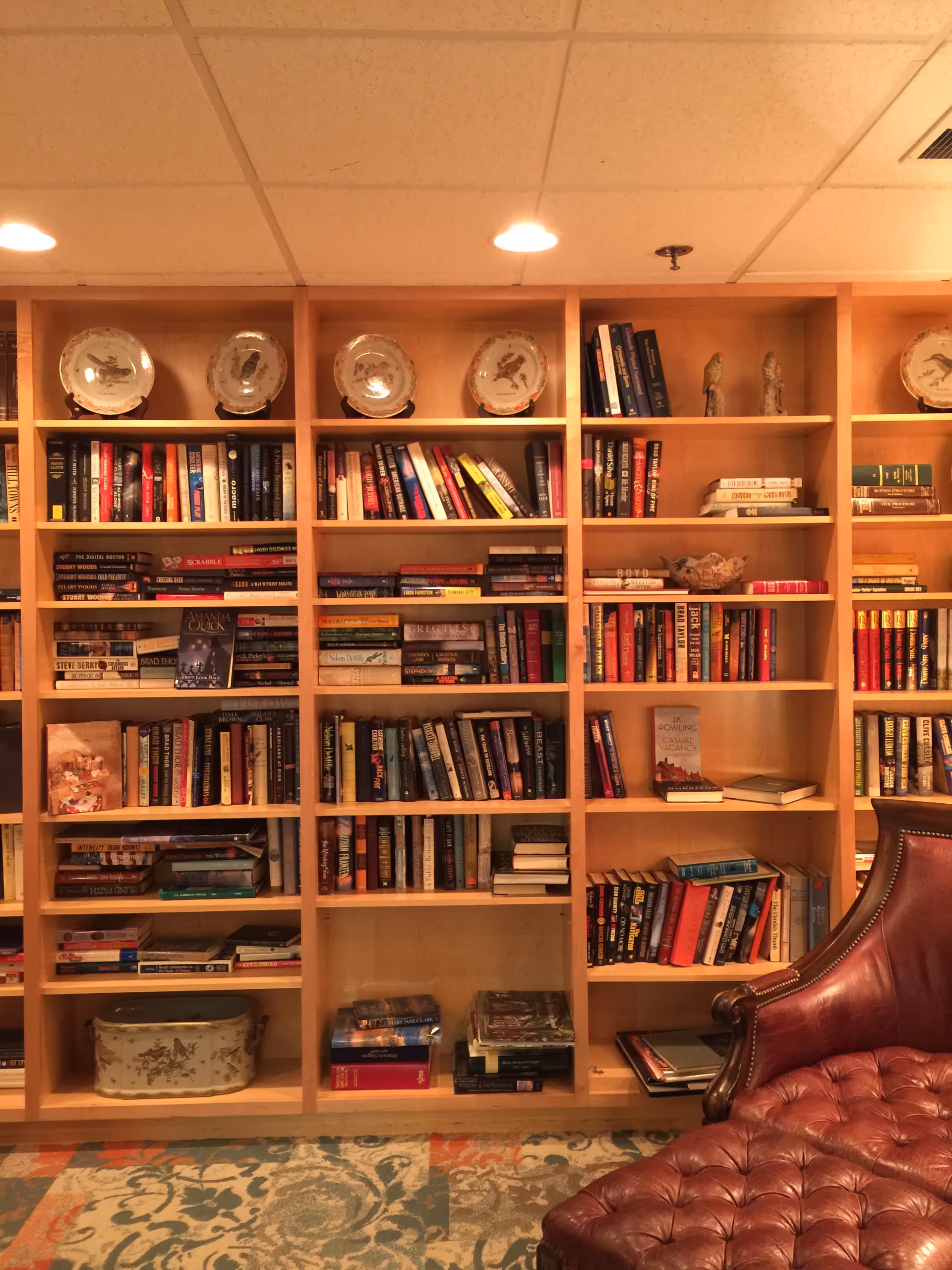 Tall wooden bookshelf filled with books and decorative plates in a lounge area.