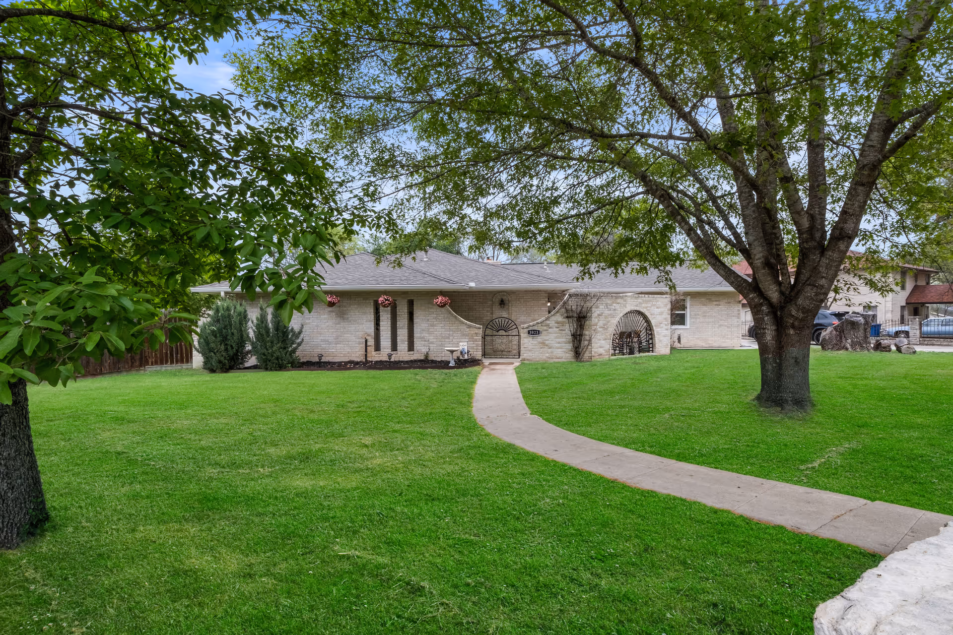 Single-story brick home with an arched entry, a curved concrete walkway, and a wide green front lawn framed by large trees.