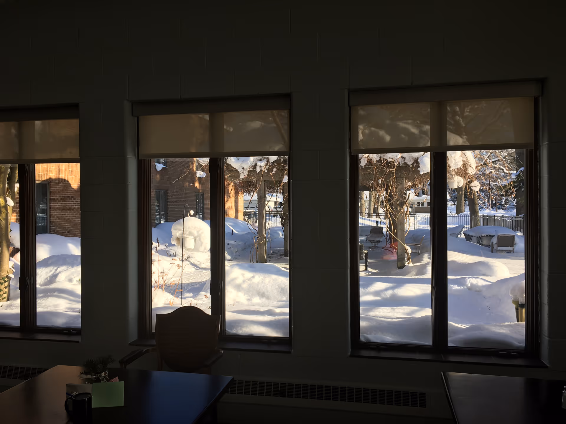 Inside a dim dining area looking out through large windows at a snowy outdoor courtyard