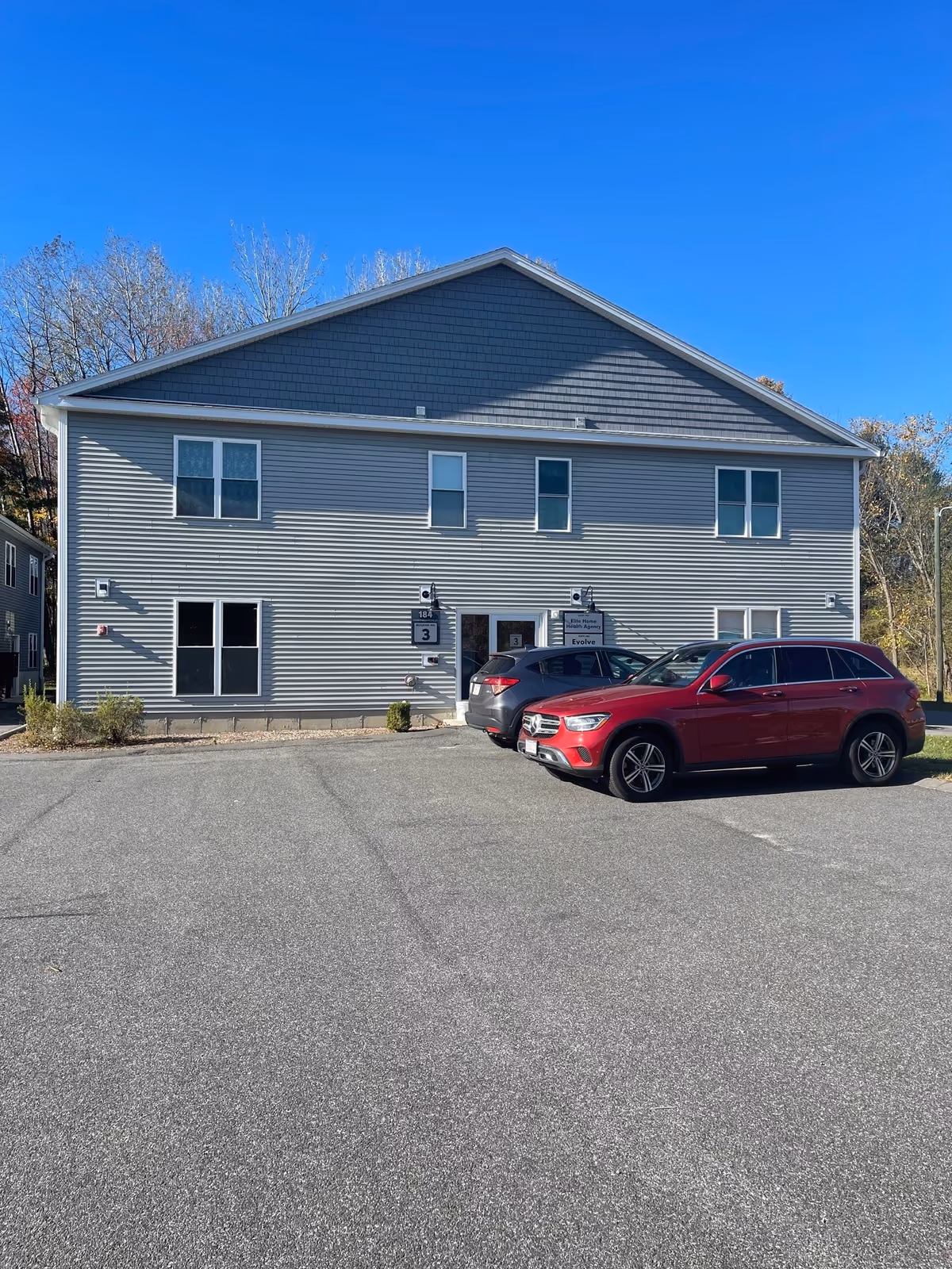 Two-story gray building with parked cars in front, blue sky overhead.