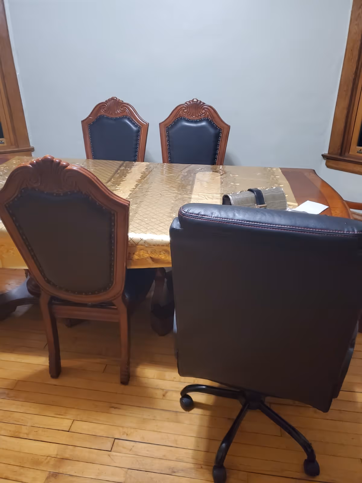 Dining room with ornate wooden chairs around a beige table and wood floor.