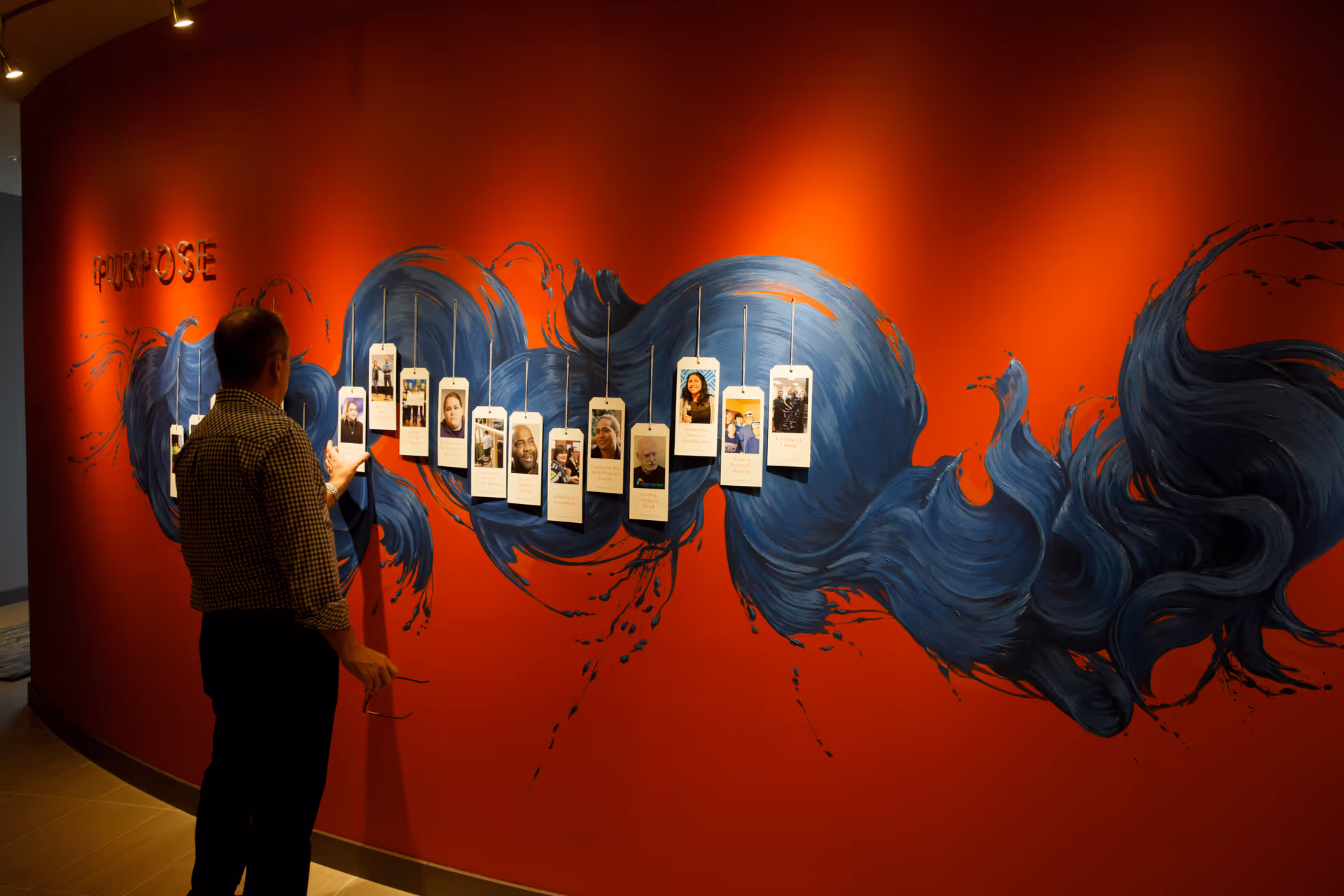 Man stands beside a red mural featuring a hanging photo display inside.