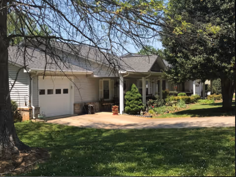 A single-story senior living facility exterior with a driveway, garage, and manicured front yard.