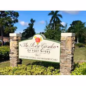 Entrance stone sign for The Rose Garden of Fort Myers surrounded by landscaping and palm trees.