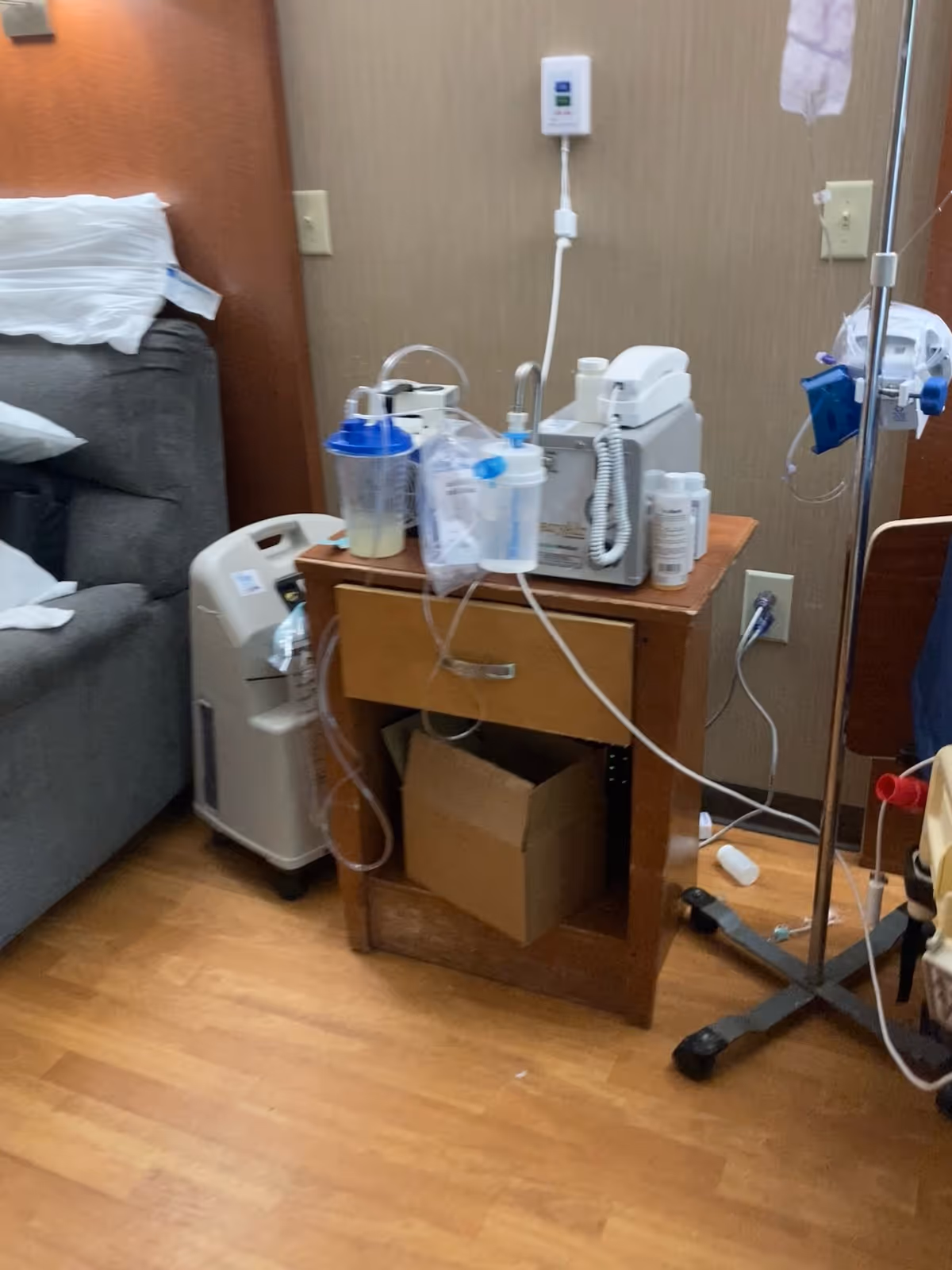 A hospital-style patient room with a bed, IV pole, and medical equipment on a wooden cart.