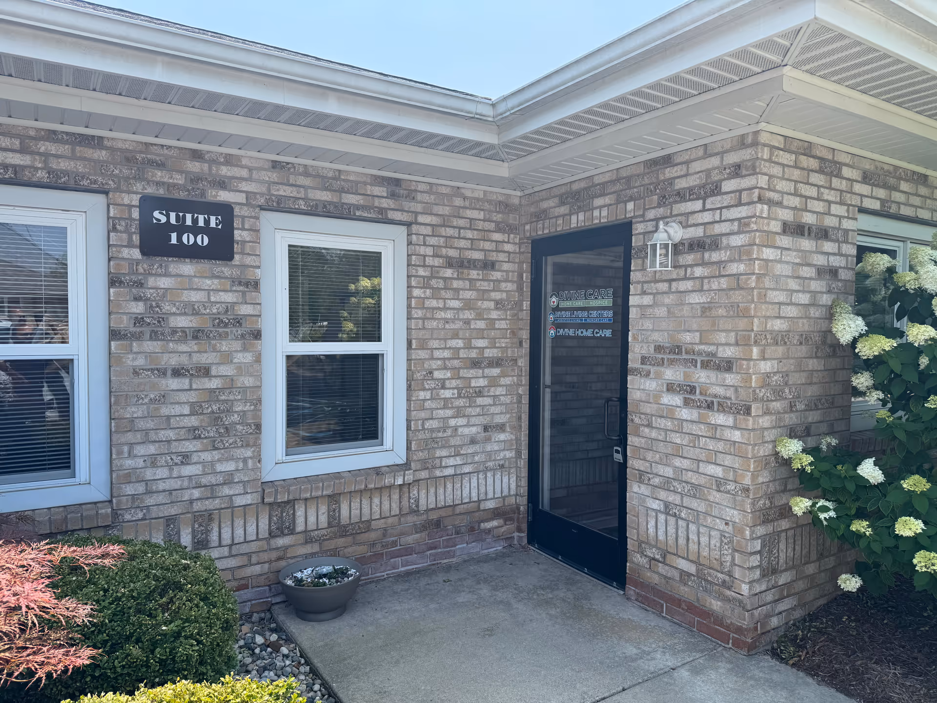 Brick exterior of a senior care facility with Suite 100 door and nearby shrubs.