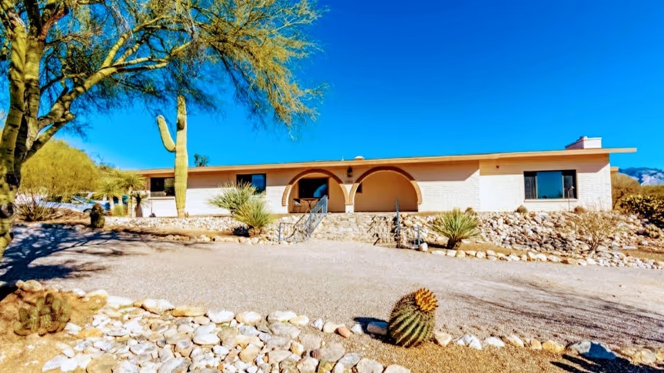 Single-story desert-style facility exterior with arches, gravel driveway, and cacti in foreground.