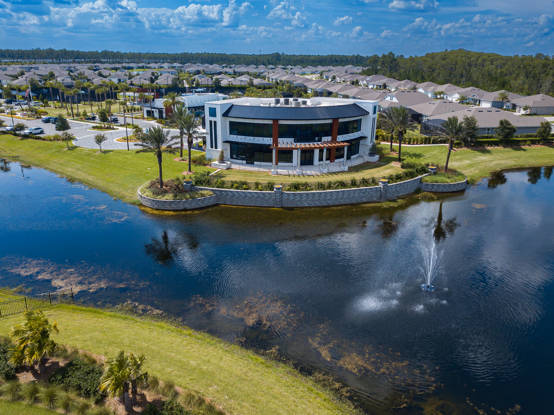 A modern, curved-front building sits on a small island surrounded by a pond and fountain.