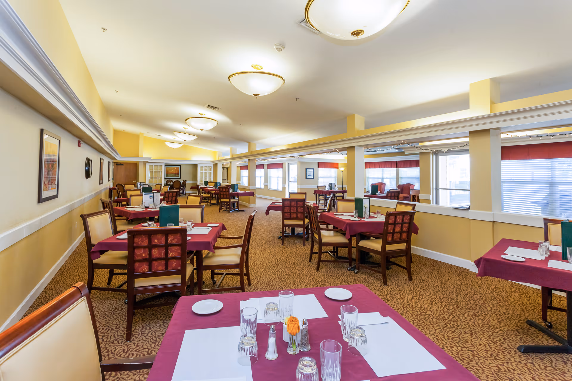Bright dining room in a senior living facility with maroon tablecloths.