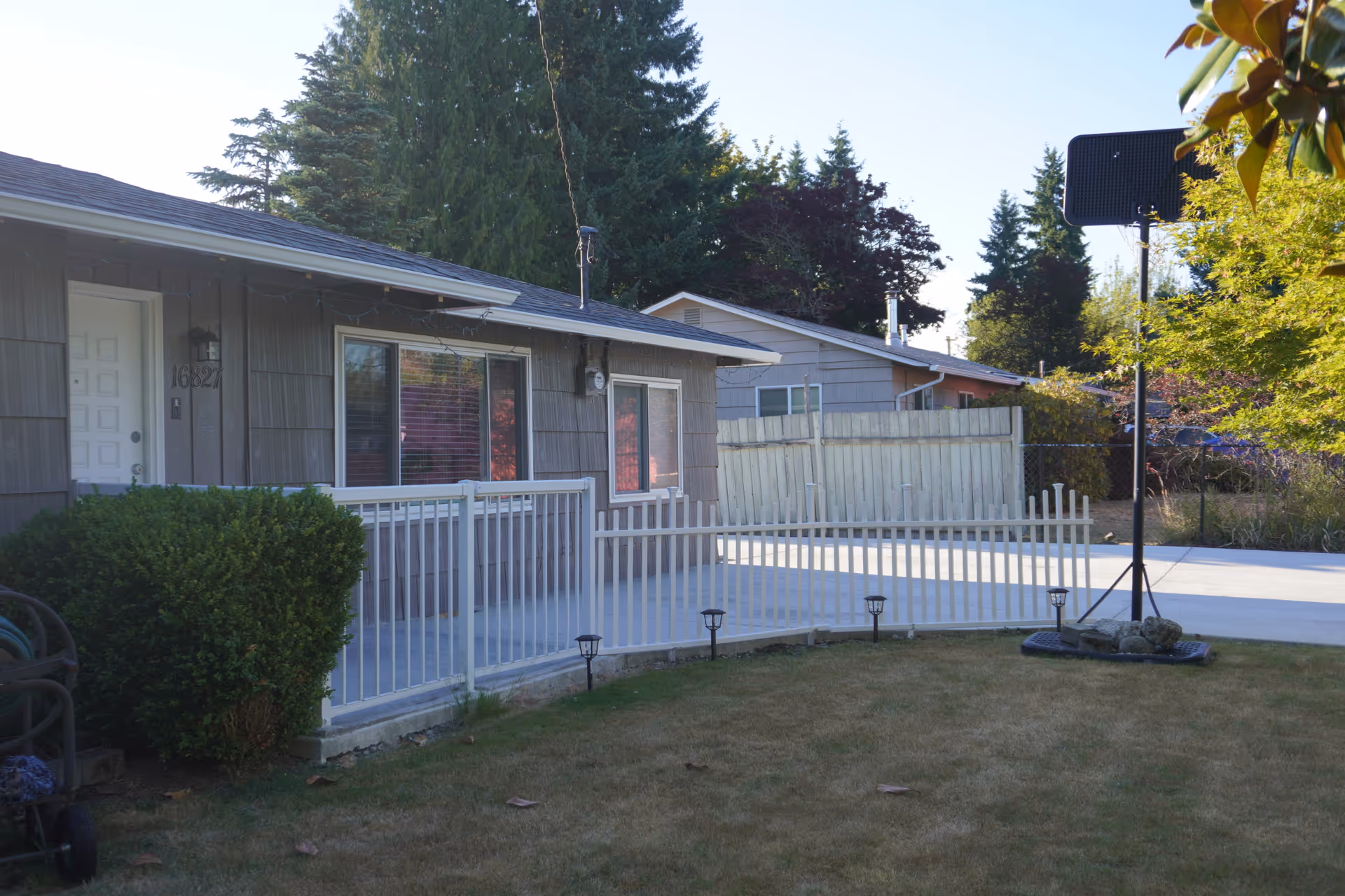 Single-story home with white railing, fenced yard, and a basketball hoop.