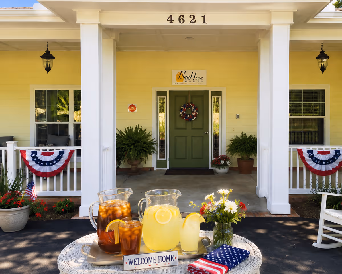 Bright yellow BeeHive Homes entrance with green door, bunting, and lemonade on the porch.