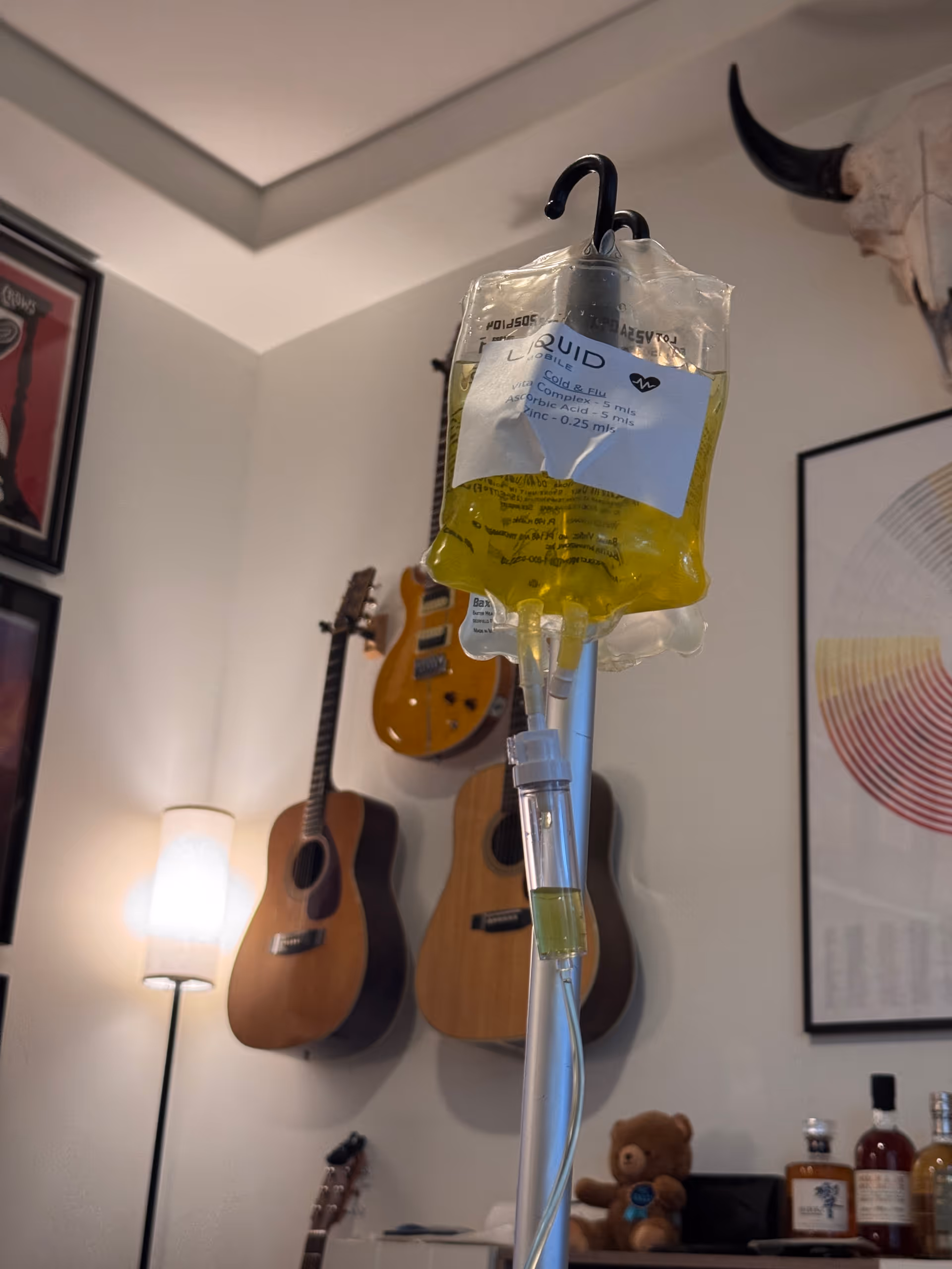 IV drip bag hangs in a cozy living room with guitars on the wall.