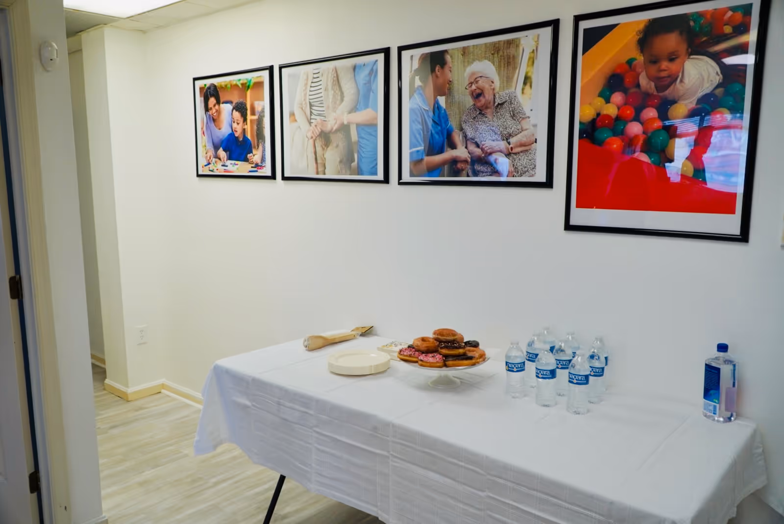 Table with donuts and bottled water along a wall of four framed photos in a corridor.