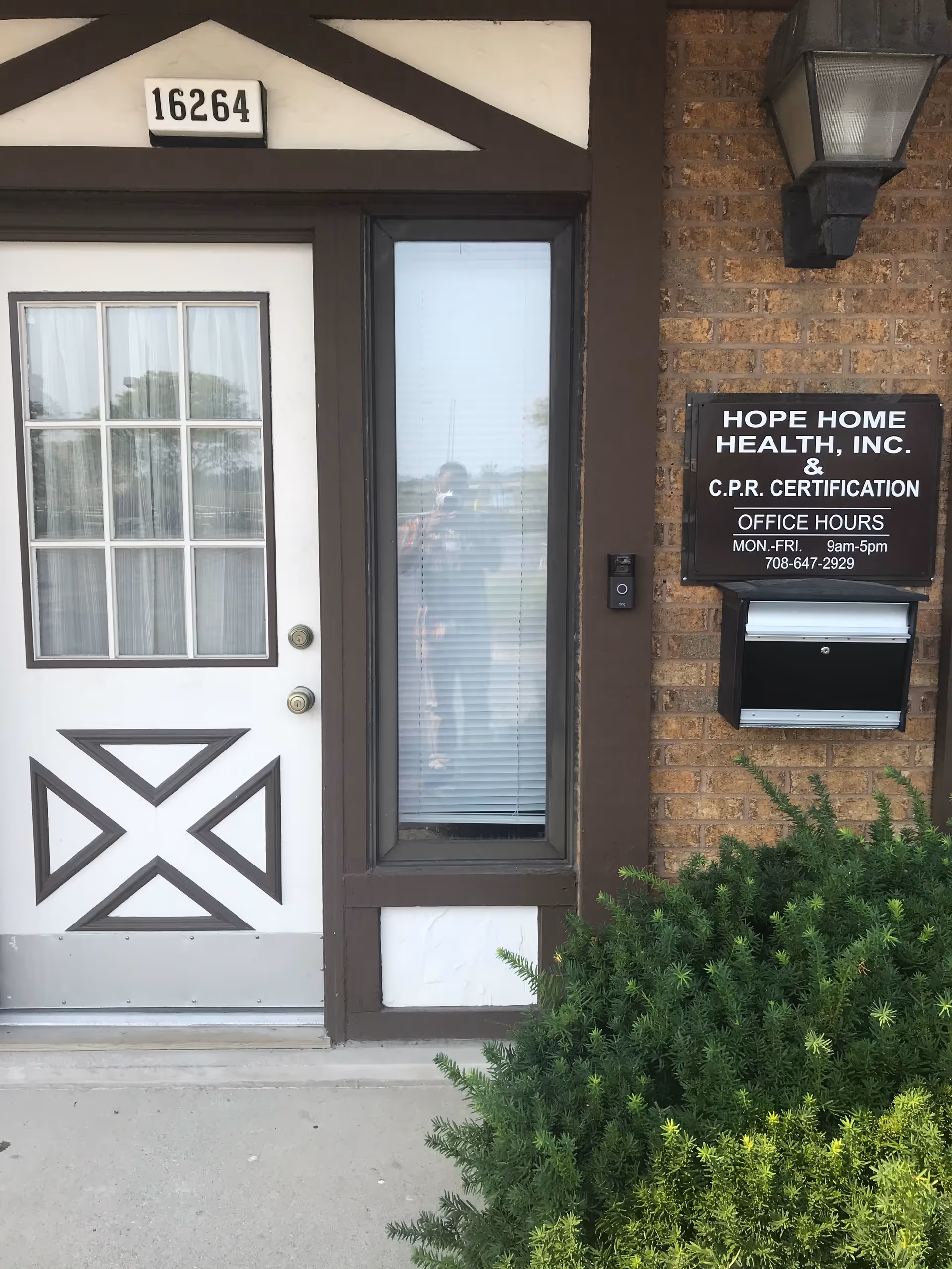 Front entrance of Hope Home Health, Inc. building with door, window, sign, and surrounding greenery.