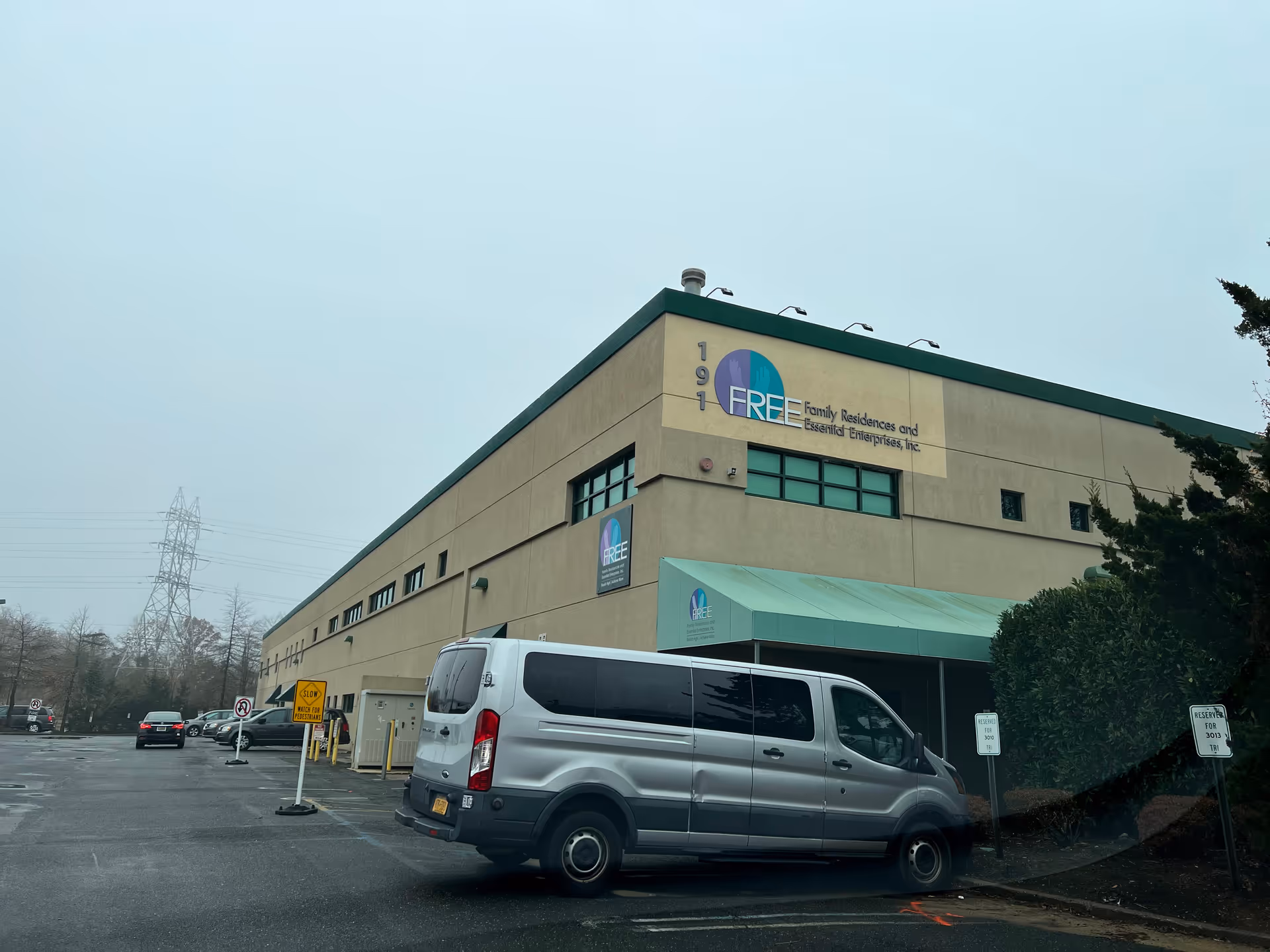 Facade of a beige facility building with FREE logo, parking lot, and a white van.