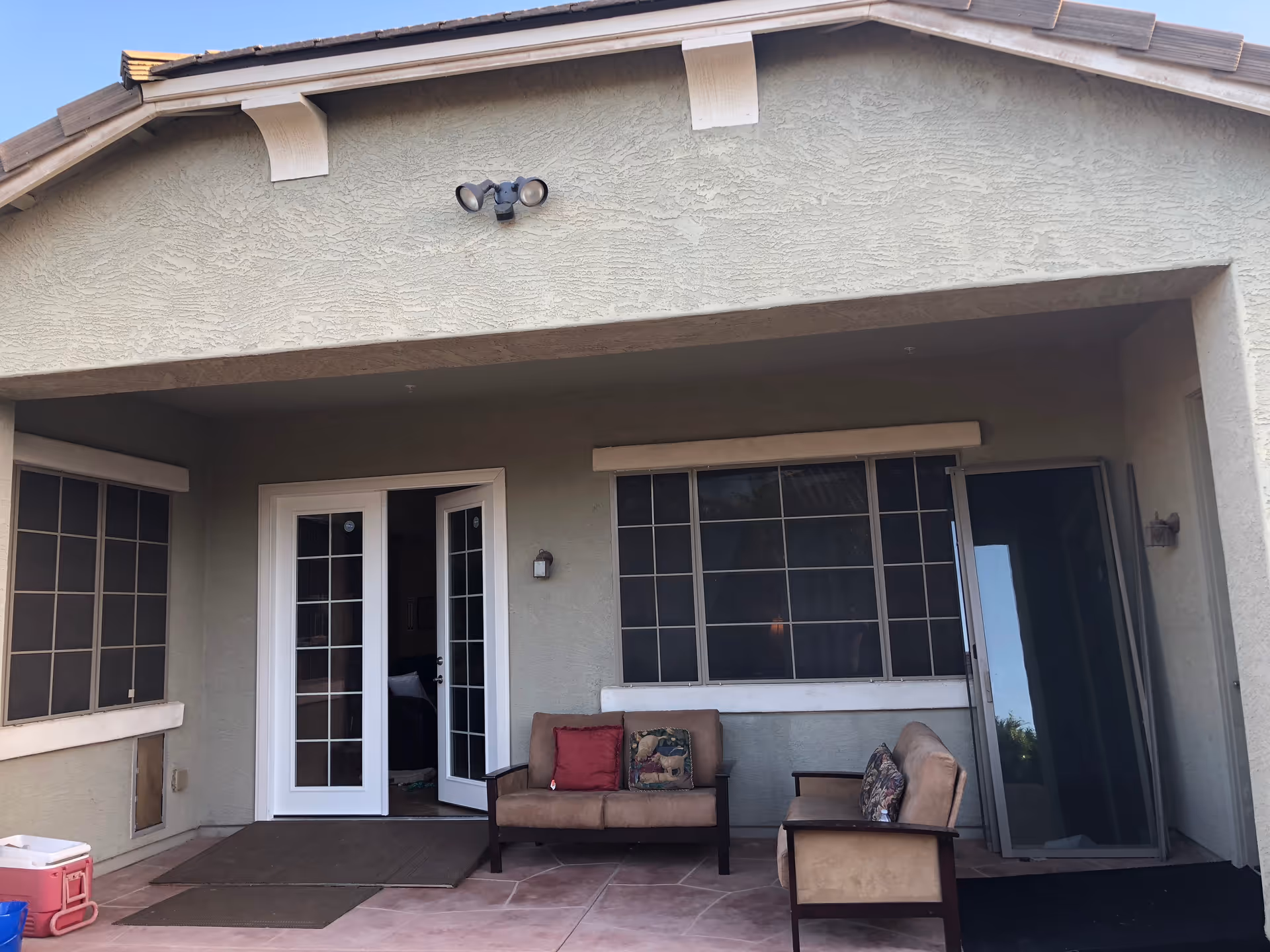 Exterior covered patio with couches and chairs facing large windows and glass doors.