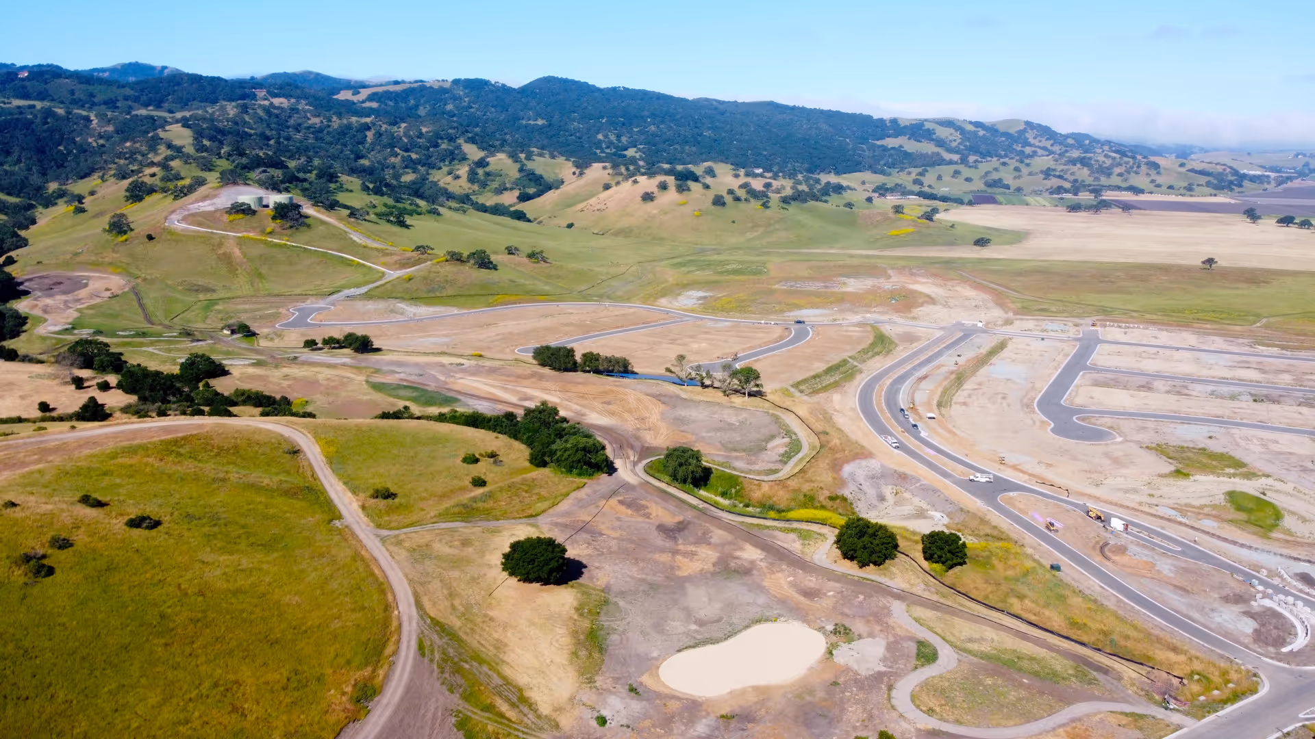 Aerial view of a hilly development site with winding roads and sparse vegetation.