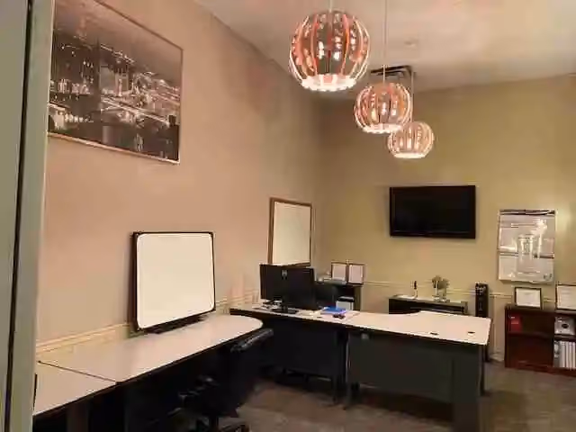 Administrative office with desks, computers, a whiteboard, and a wall-mounted TV in a bright room.