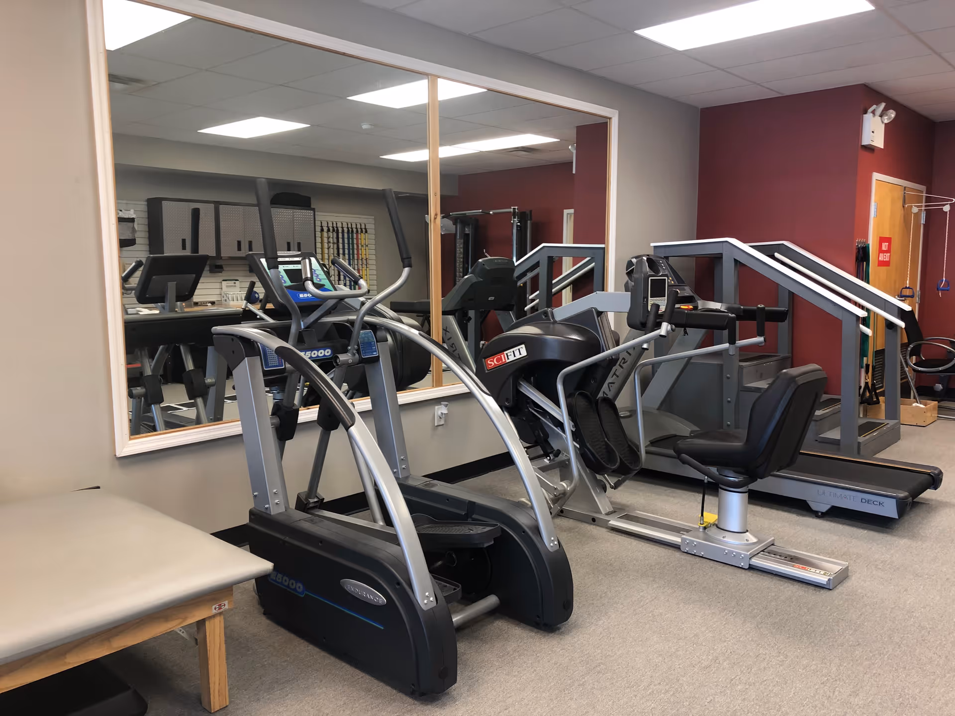 Interior fitness room with treadmills, ellipticals, and a mirrored wall.