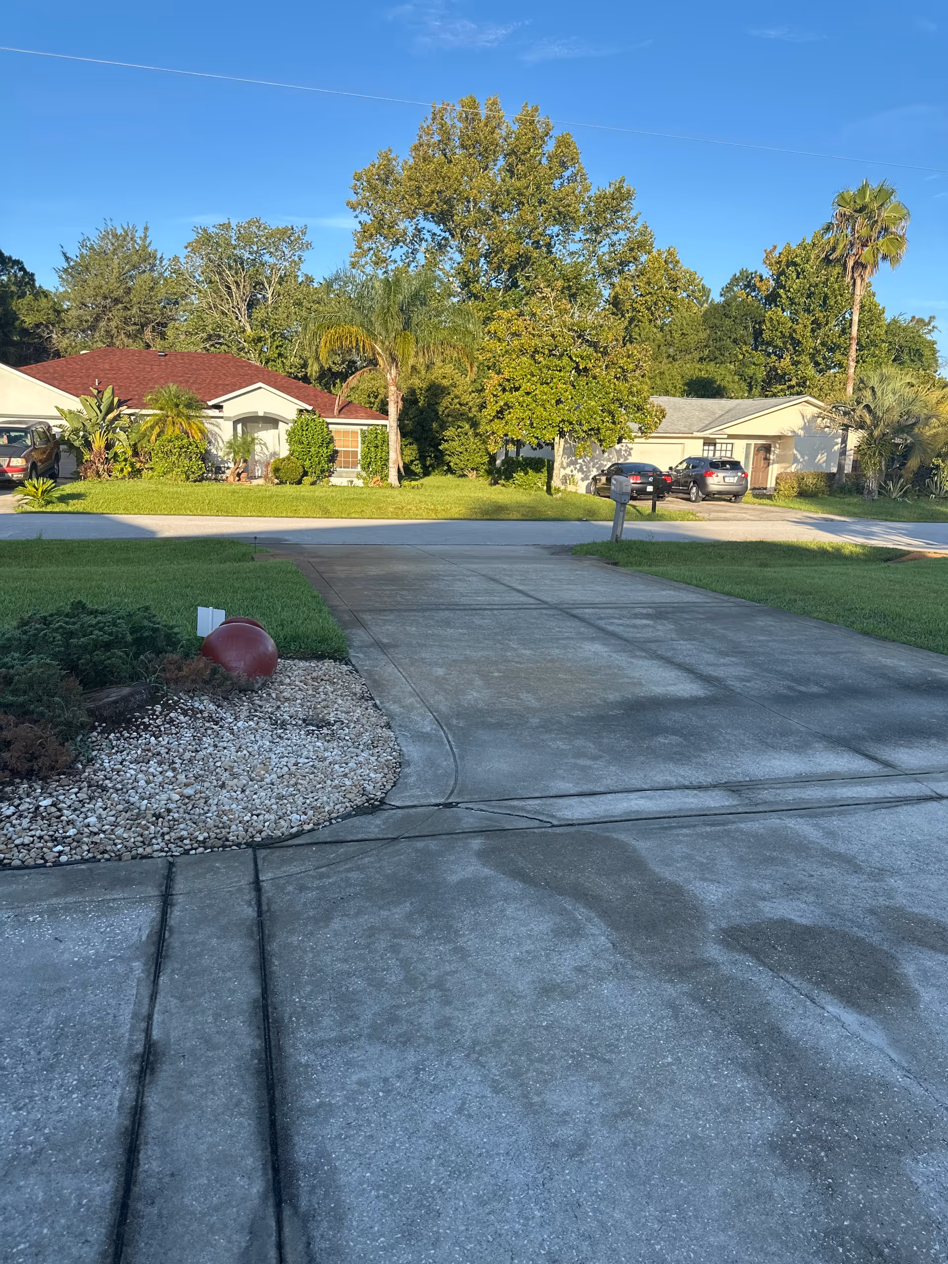 Wide suburban street with driveways, cars, and trees in front of single-family homes.