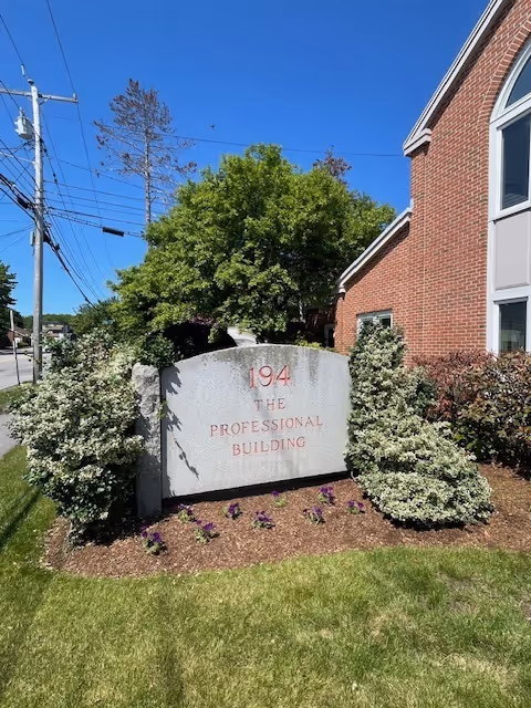 Brick building exterior with a stone sign and neatly landscaped shrubs.