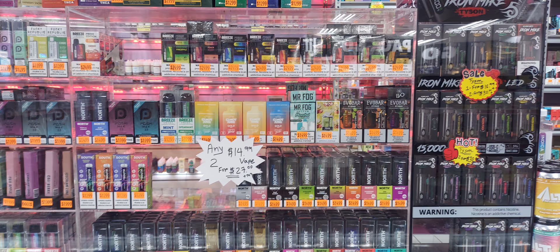Interior storefront with shelves packed with vape products and bright pink lighting.