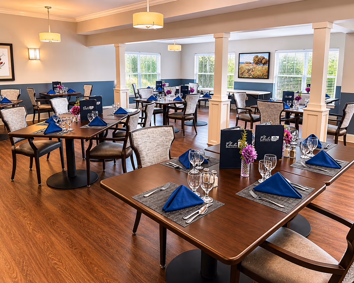 Bright, spacious dining room with brown tables, blue napkins, glassware, and centerpieces.