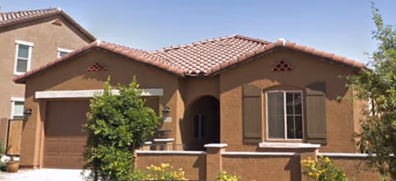 Single-story stucco house with a red tile roof, attached garage, front courtyard wall, and small landscaped shrubs.