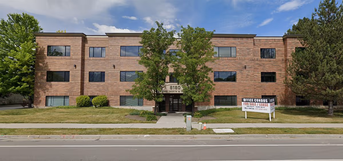 Brick senior living facility exterior with trees, walkway, and a street in front