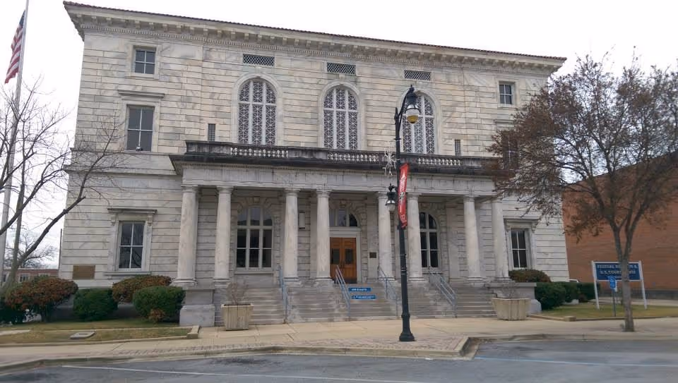 Front view of a large stone building with columns, steps, and arched windows.