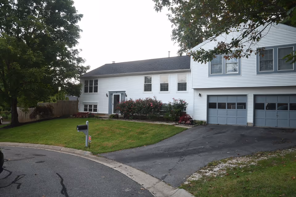 White two-story senior living facility with driveway, garage doors, and landscaped front yard.