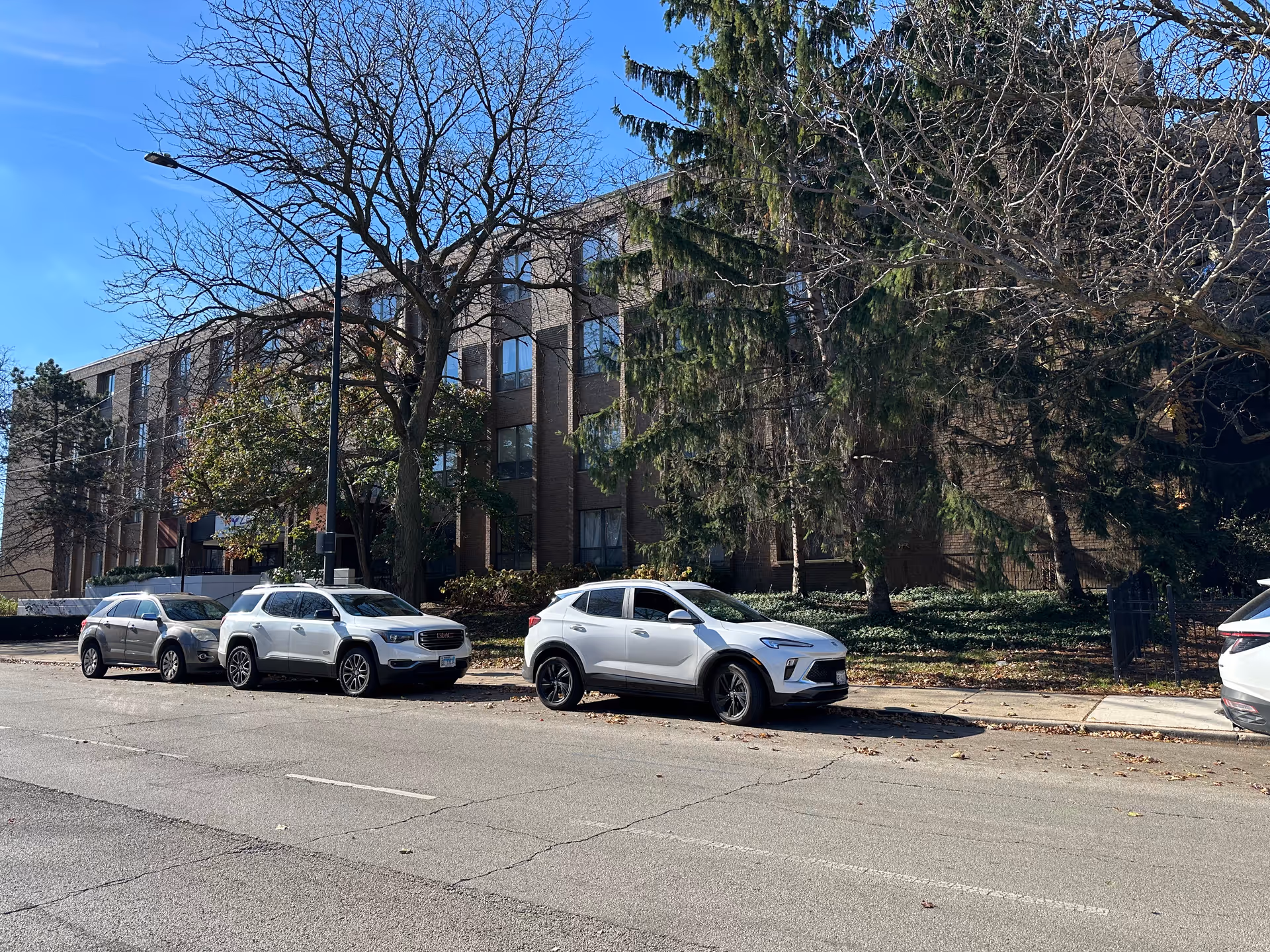 Street view of a multi-story brick residential building with trees and several cars parked along the curb.