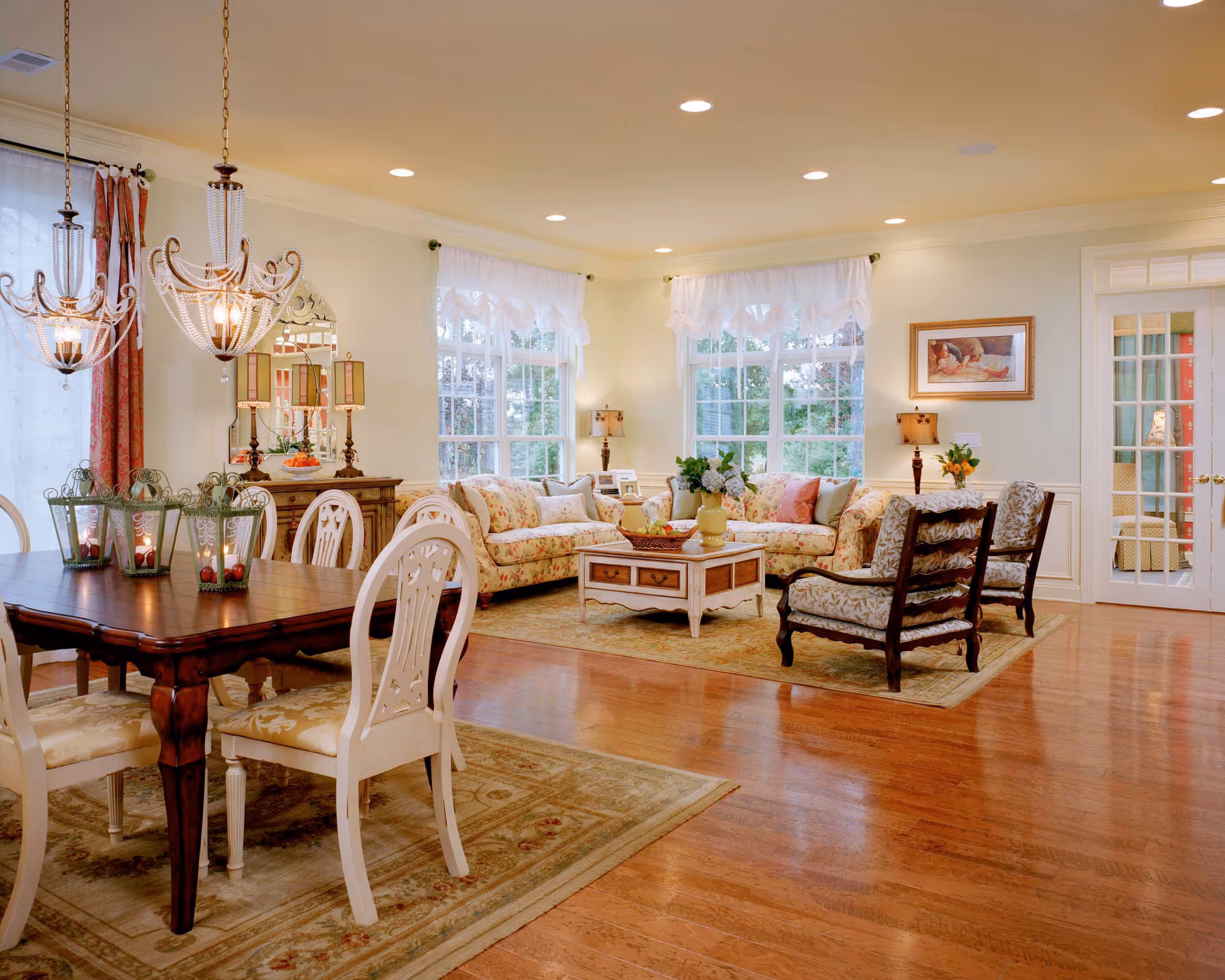 Bright, elegantly furnished living room with floral sofas, chairs, coffee table, and large windows.