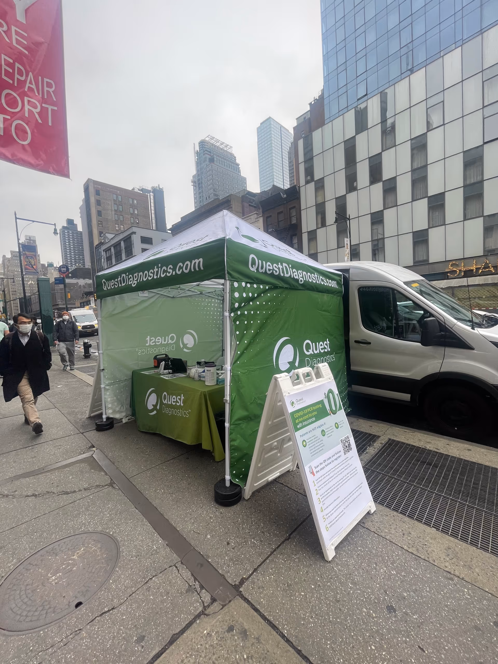 Green Quest Diagnostics testing tent on a city sidewalk beside a white van