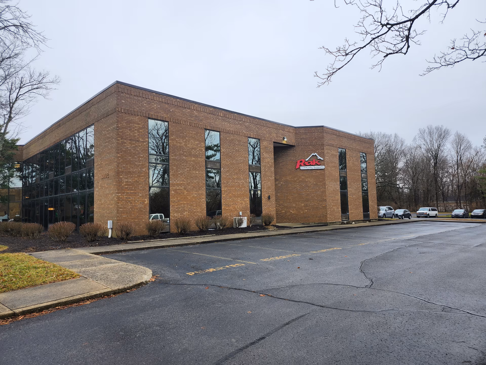 Brick senior living building with large glass windows and a parking lot in front