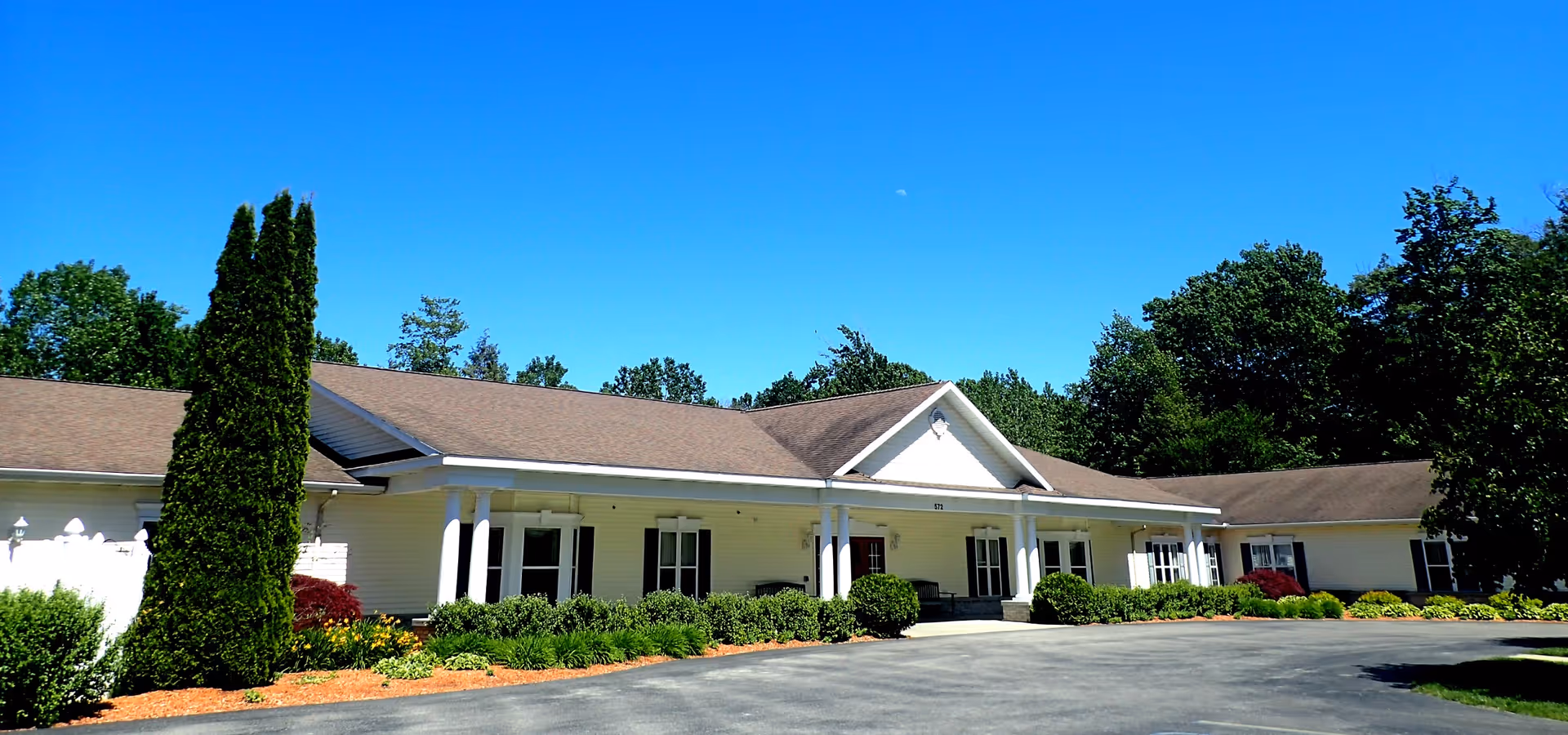 Single-story senior living facility exterior with a covered entrance and landscaped shrubs.