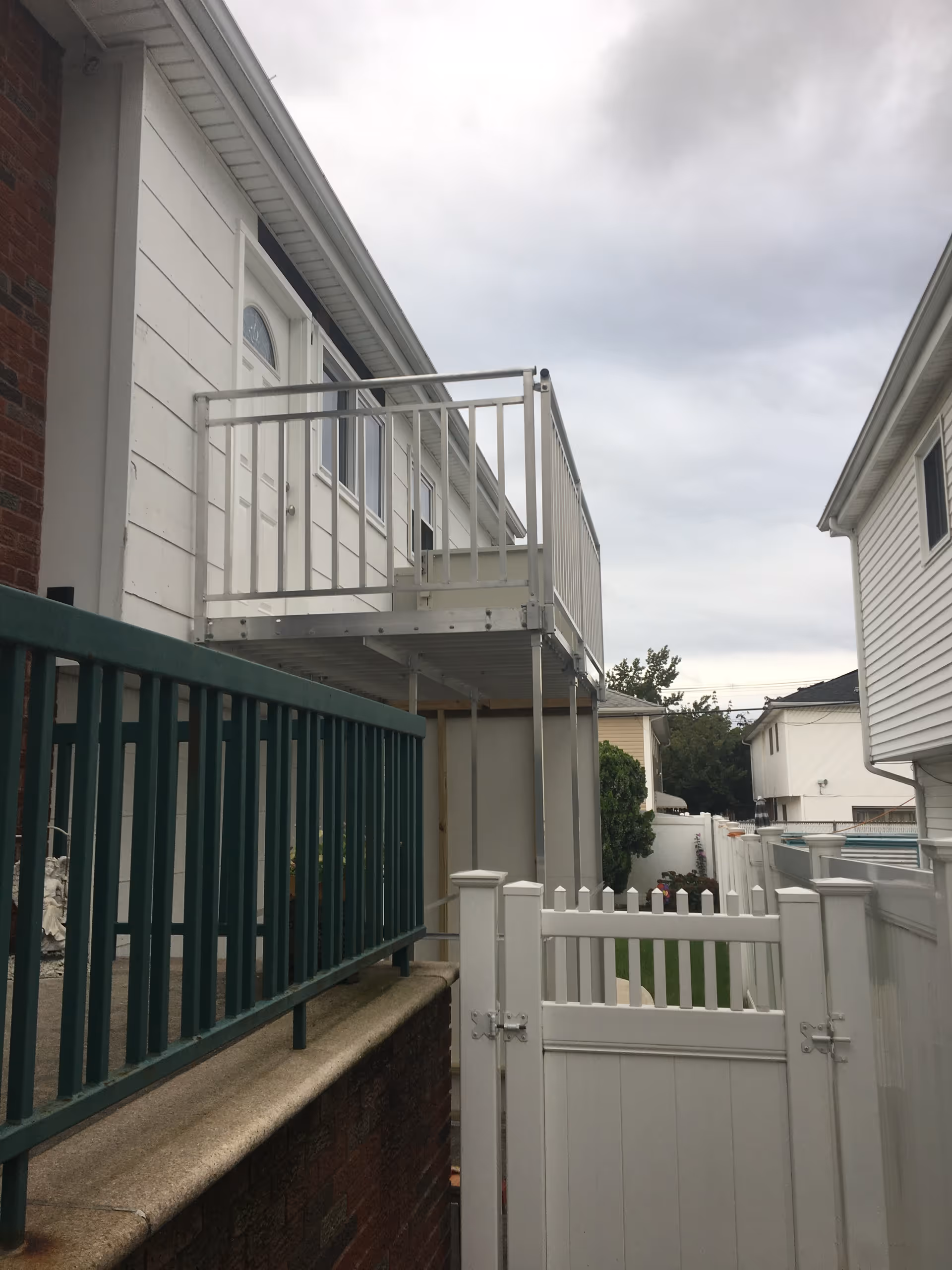 White two-story exterior with a balcony, railing, and fenced walkway.