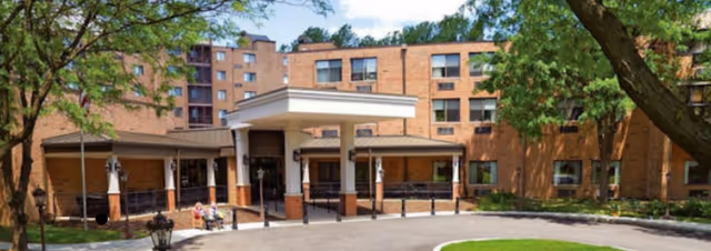 Brick building with a canopy entrance for a senior living community, surrounded by trees.
