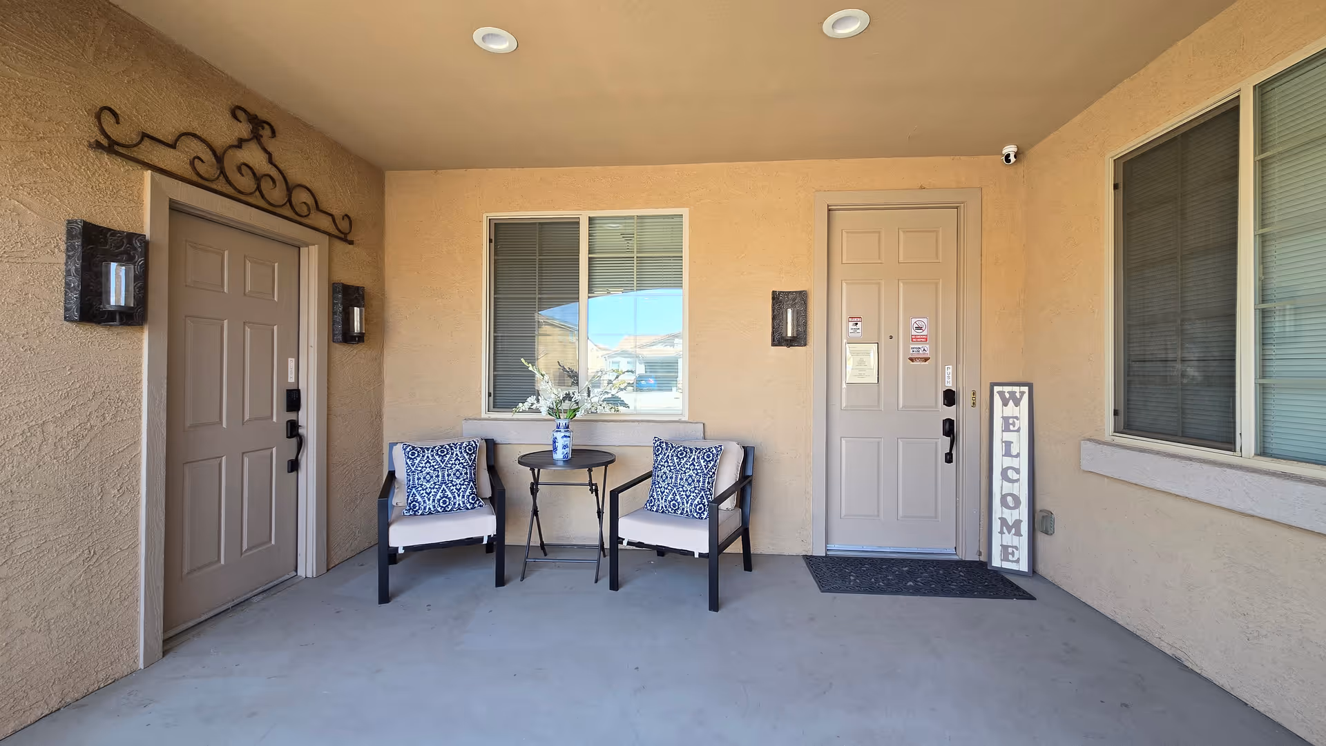 Covered entrance porch with two chairs, a small table, and welcome sign.