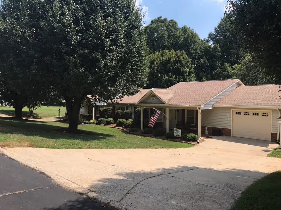 Exterior of a single-story senior living home with flag, driveway, and trees.