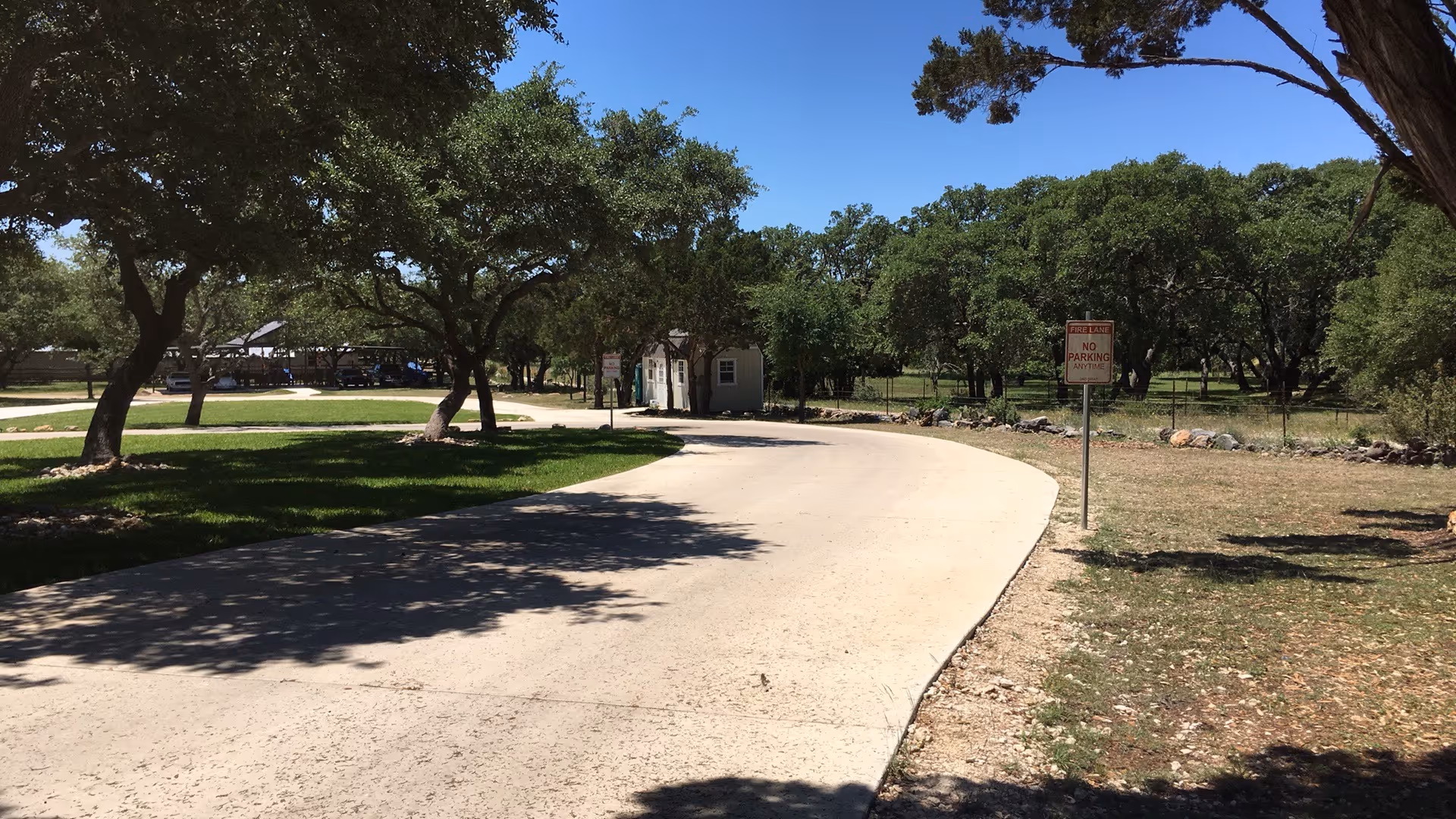 Curved driveway winds through trees toward a facility entrance under clear blue sky.