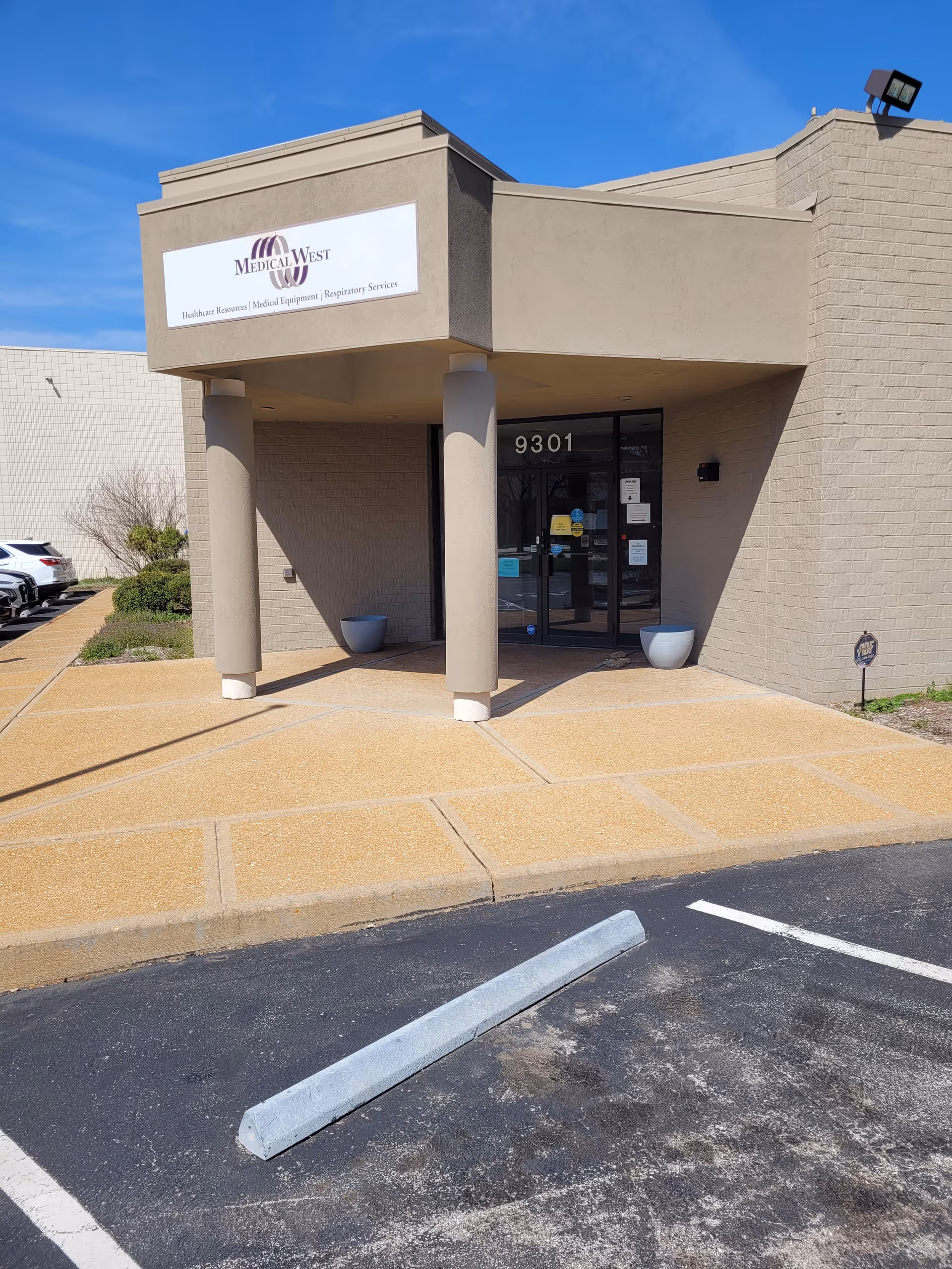 Front entrance of Medical West facility with sign, columns, glass doors, and parking.