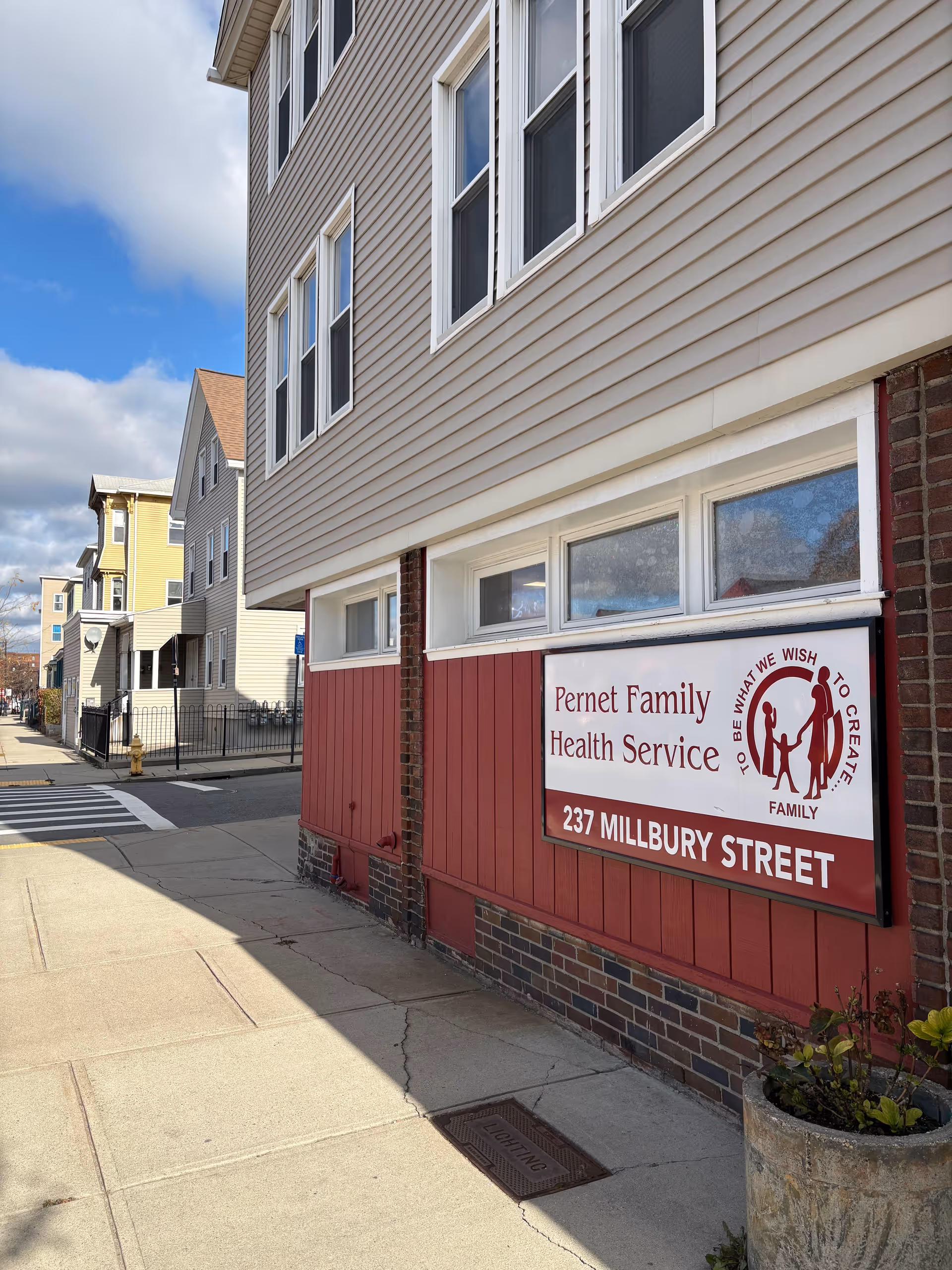 Beige building with a red and white sign for Pernet Family Health Service on Millbury Street.